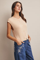 Woman wearing a beige ribbed top and blue jeans with floral embroidery on a plain background