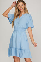 Woman wearing a light blue dress with ruffled hem on a plain background