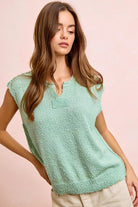 Woman wearing a light green knitted top against a pink background