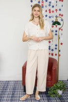Woman in a white lace top and beige pants standing in front of a decorative wall with star patterns.