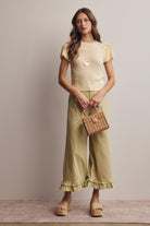 Woman wearing a yellow top and green pants holding a woven bag against a neutral background