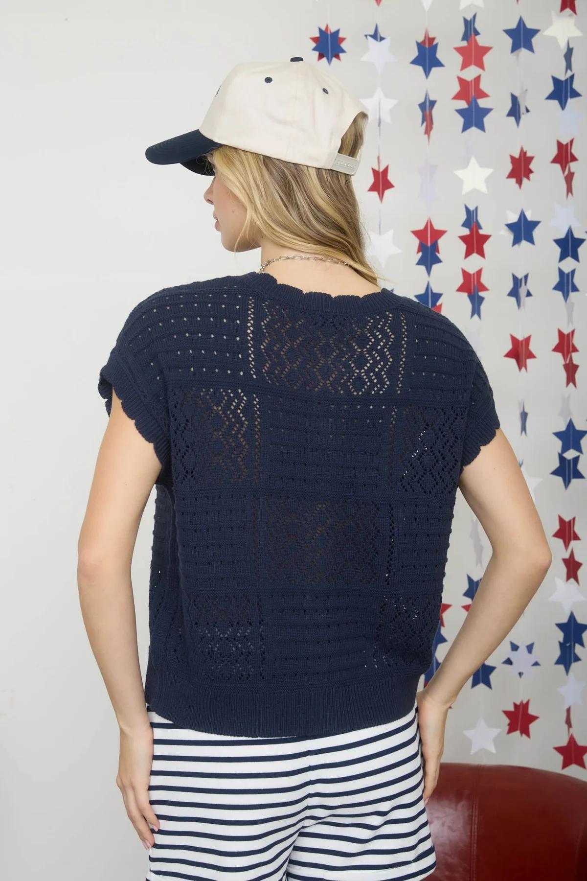Woman wearing a navy blue crochet top with a white cap against a red, white, and blue star-patterned wall.