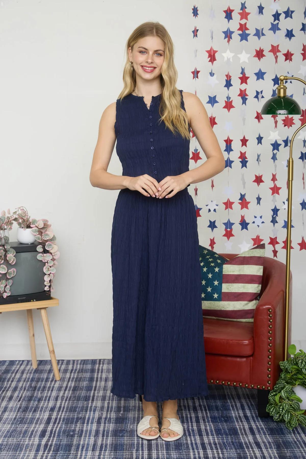 Woman in a navy dress standing in a room with a decorative wall and furniture.
