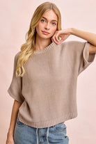 Woman wearing a beige sweater and blue jeans against a pink background