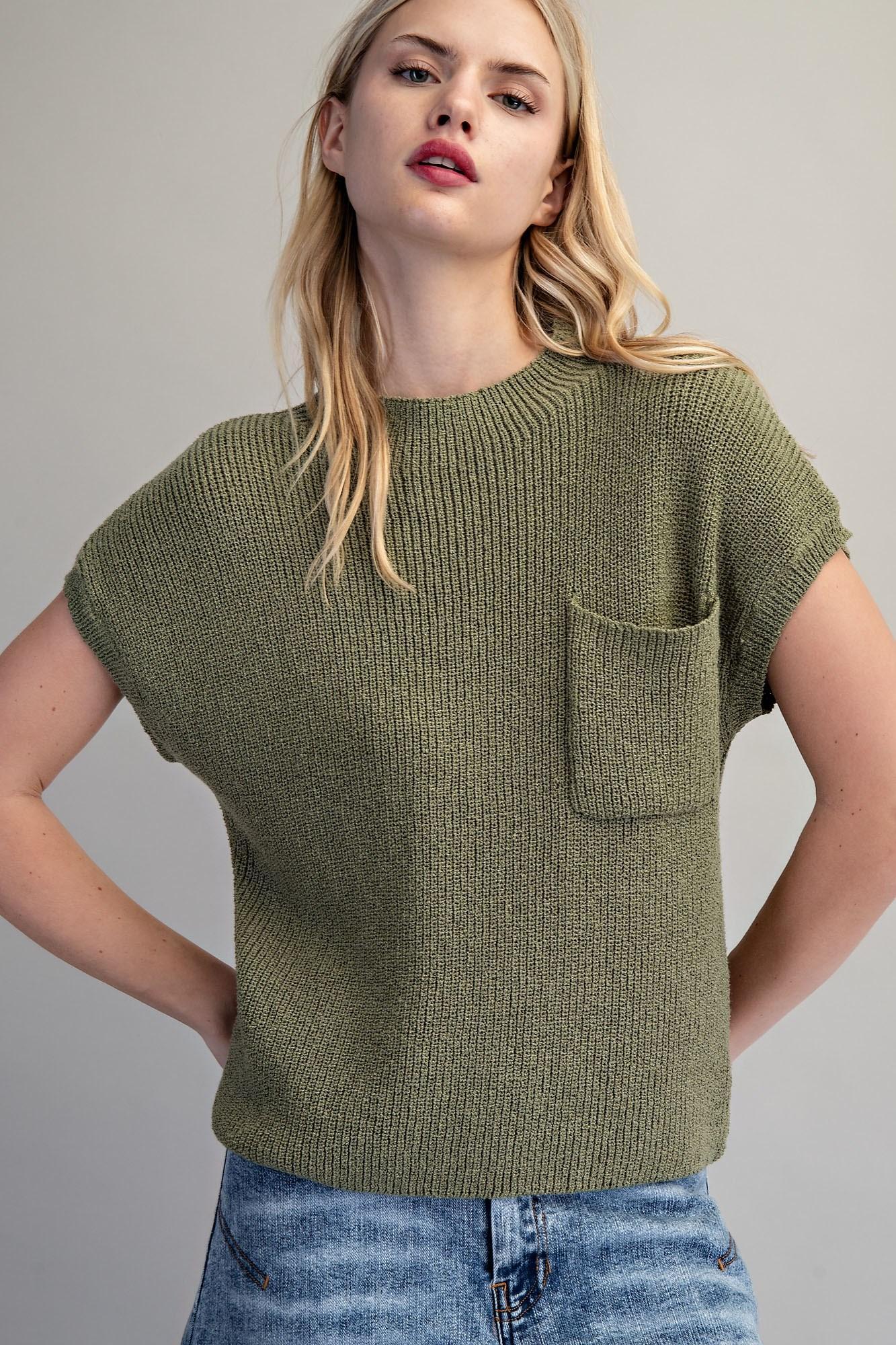 Woman wearing a green knitted t-shirt with a pocket against a plain background