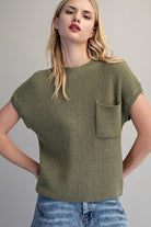 Woman wearing a green knitted t-shirt with a pocket against a plain background