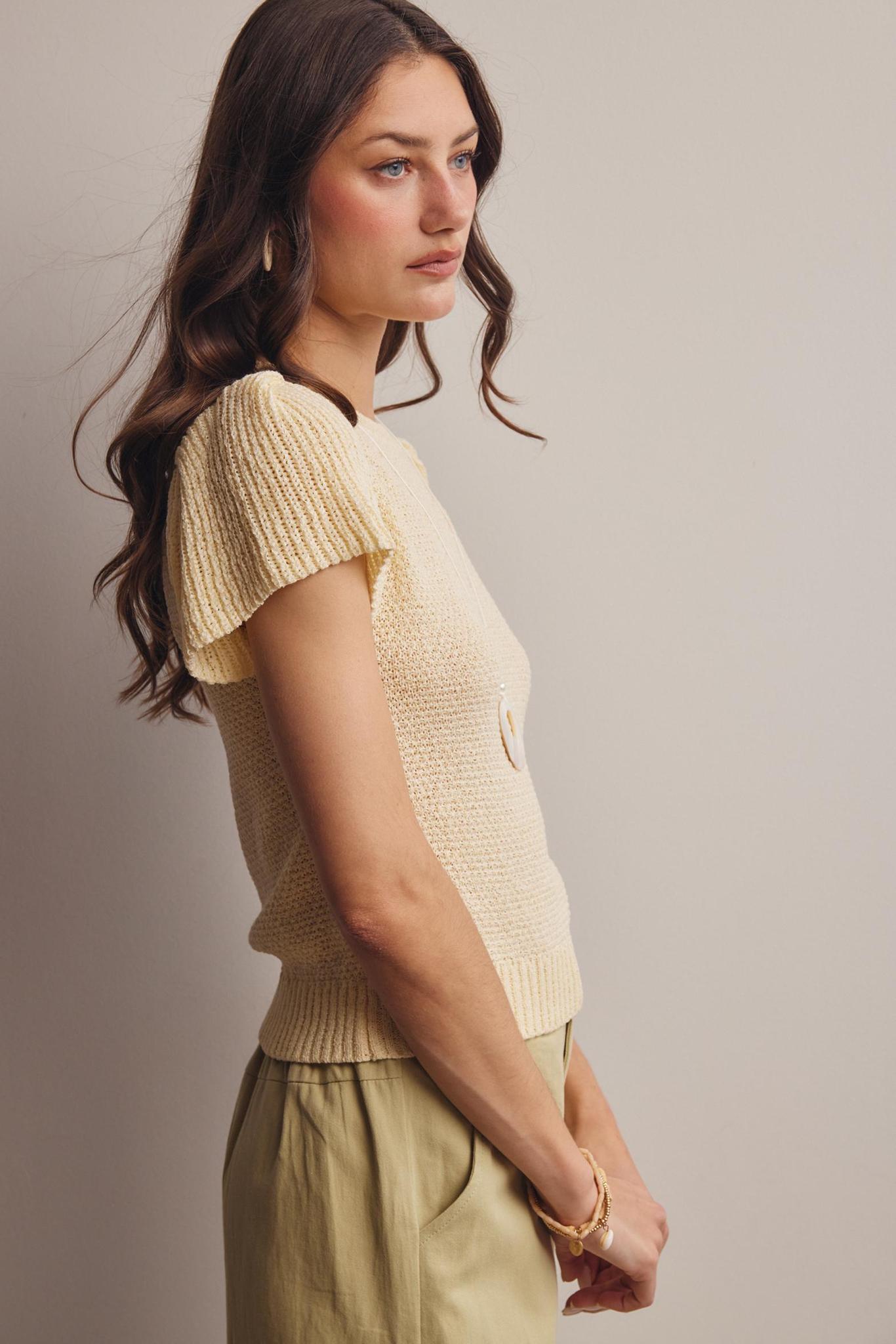 Woman wearing a beige knitted top and pants against a plain background