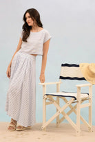 Woman in striped outfit standing next to a director's chair with a straw hat on a light blue background