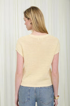 Woman wearing a light yellow crochet top and blue jeans against a white background