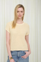 Woman wearing a yellow textured top and blue jeans against a white background