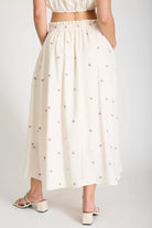 Person wearing a white skirt with small patterns on a plain background