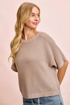 Woman wearing a beige poncho against a pink background