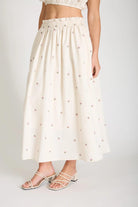 Person wearing a white skirt with small patterns on a plain background