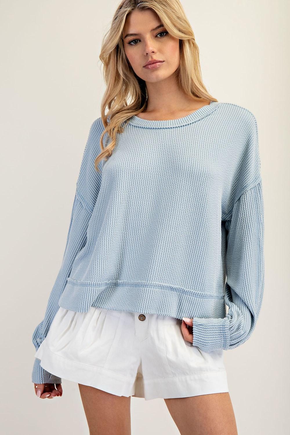 Woman wearing a light blue sweater and white shorts on a plain background