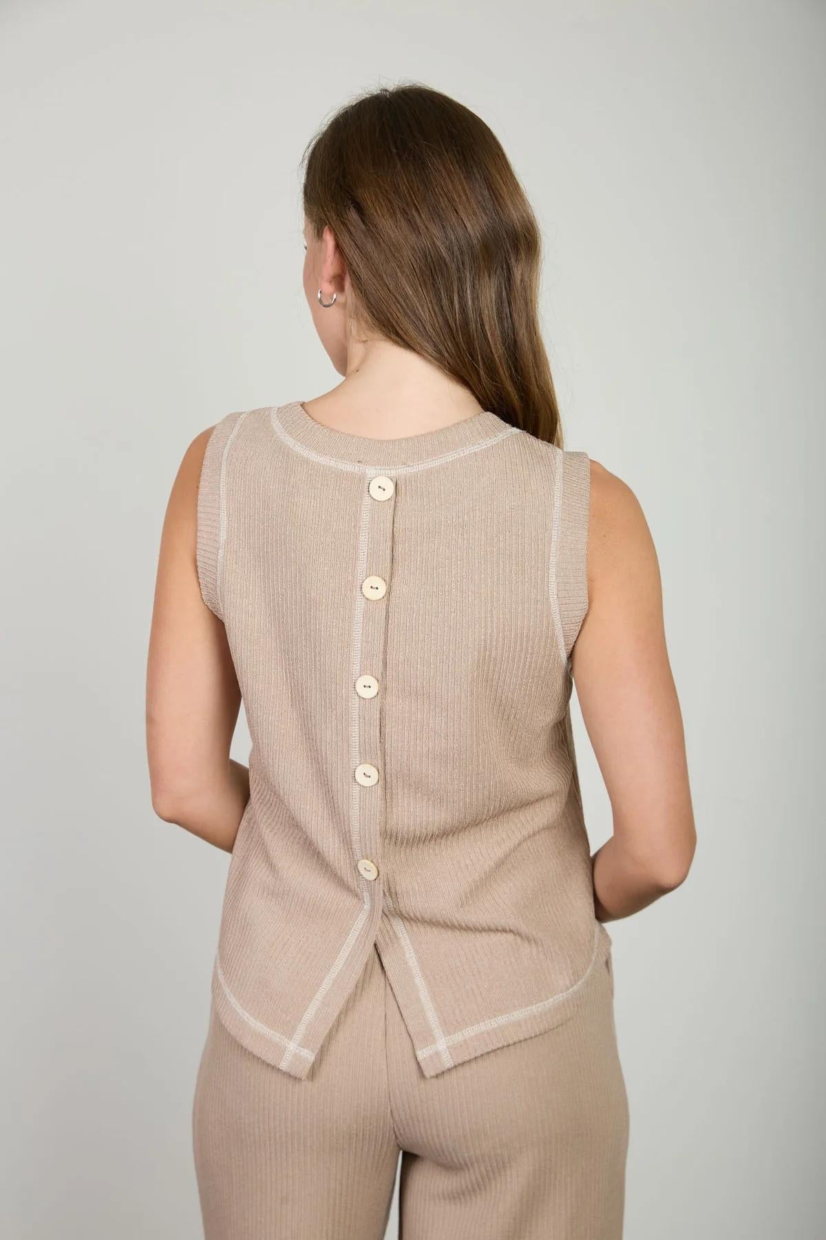 Woman wearing a beige sleeveless button-up top against a plain background