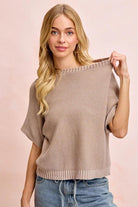 Woman wearing a beige sweater and blue jeans against a pink background