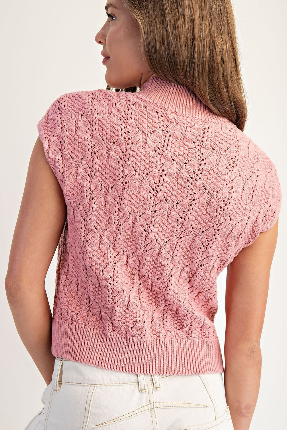 Pink knitted vest worn by a person on a white background