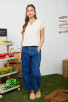 Woman in a white top and blue jeans standing in a produce section with fruits and vegetables.