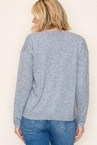 Person wearing a gray long-sleeve top and blue jeans against a beige background