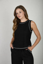 Woman wearing a black sleeveless top and pants with white trim on a gray background