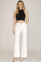 Woman wearing a black crop top and white pants on a plain background