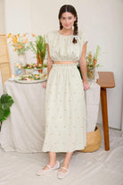 Woman in a light green dress standing in a room with a table and decorative items.