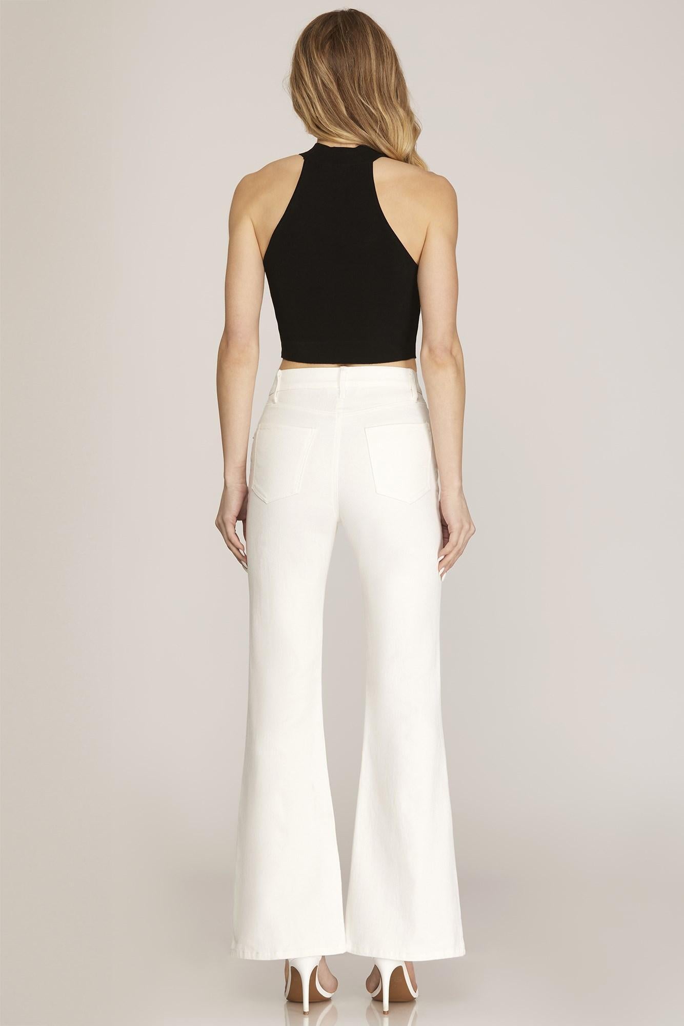 Woman wearing a black top and white pants on a plain background