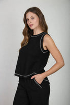 Woman wearing a black sleeveless top with white trim on a plain background