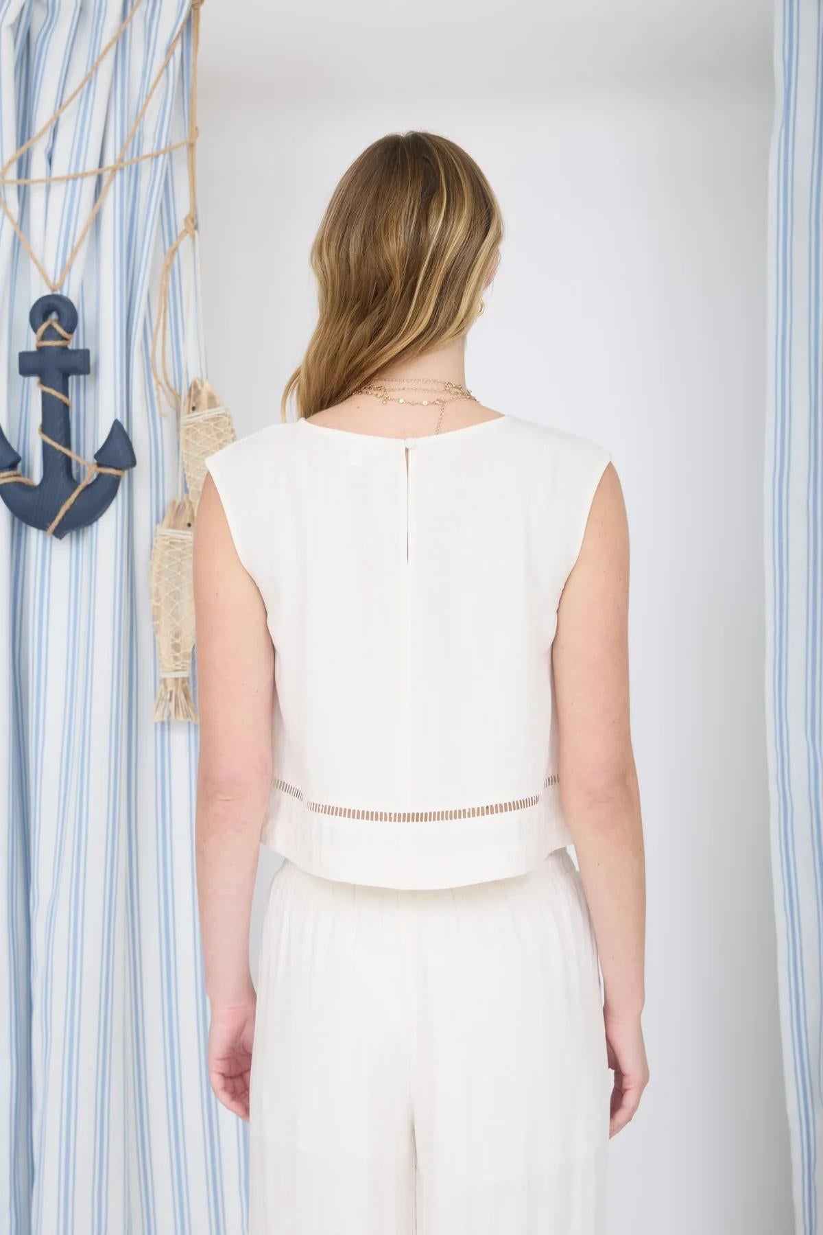 Woman wearing a white sleeveless top and pants against a striped blue and white background.