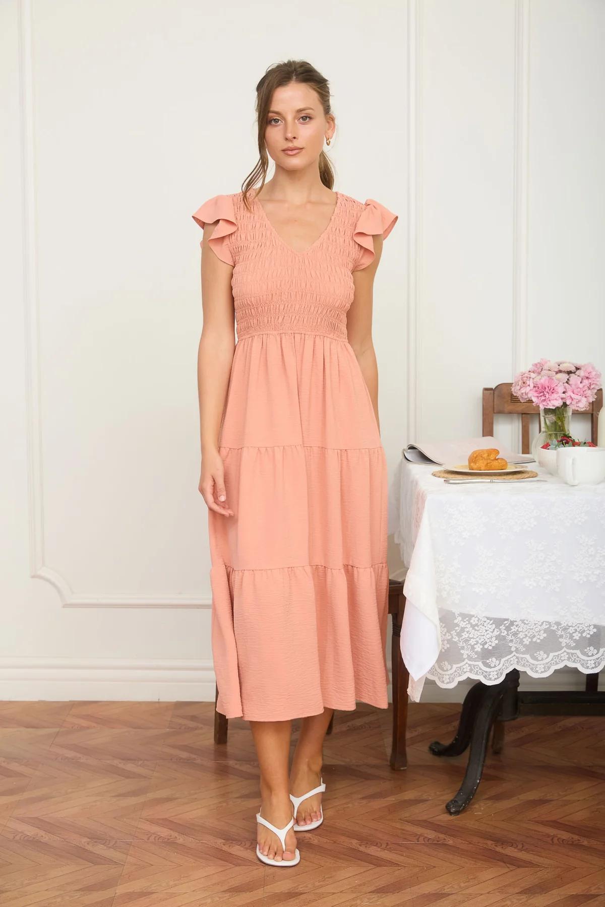 Woman in a peach dress standing in a room with a table and flowers.