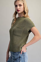 Woman wearing a green knitted top with a pocket against a gray background