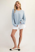 Woman wearing a light blue sweater and white shorts on a plain background