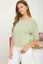 Woman wearing a light green sweater and white pants sitting at a table with a plate of food.