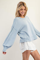Woman wearing a light blue sweater and white shorts on a plain background