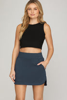 Woman wearing a black sleeveless top and navy skirt on a plain background