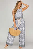 Woman wearing a patterned outfit holding a straw bag on a plain background