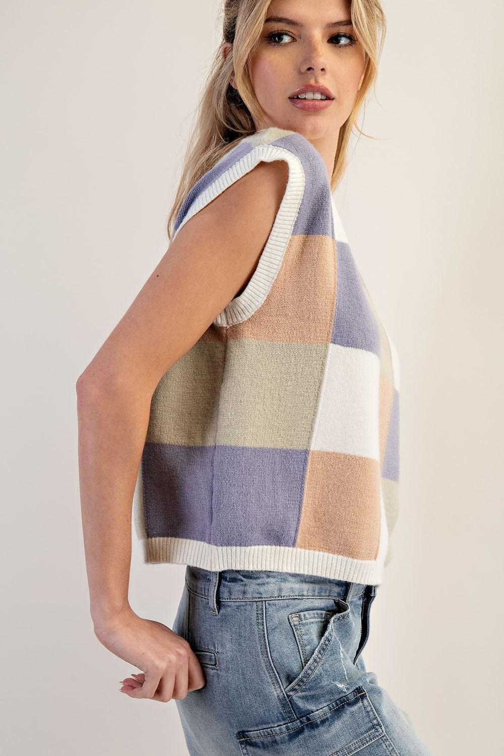 Woman wearing a sleeveless, multicolored checkered sweater against a plain background