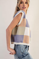 Woman wearing a sleeveless, multicolored checkered sweater against a plain background