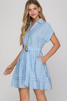 Woman wearing a blue and white striped dress with a belt on a plain background