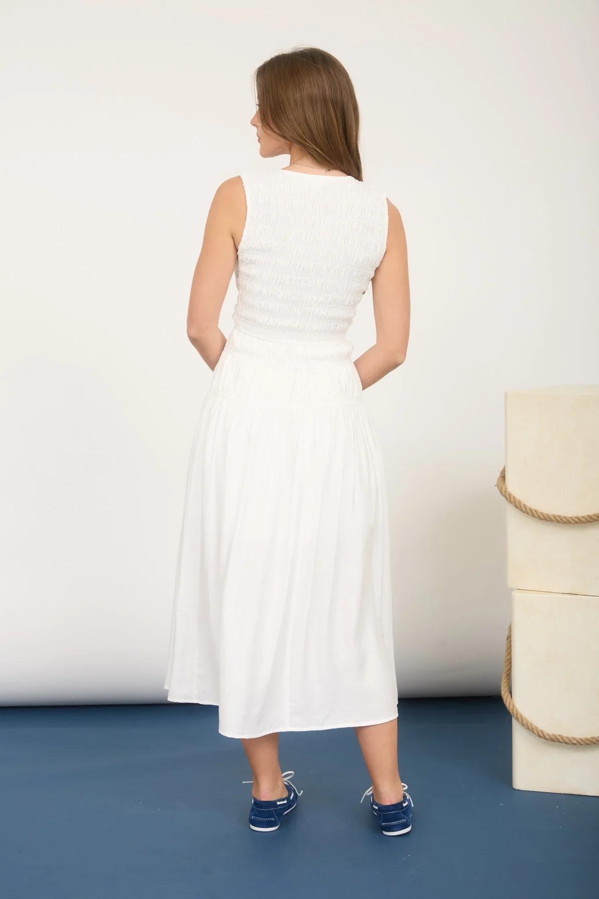 Woman wearing a white dress standing against a white wall with a blue floor.