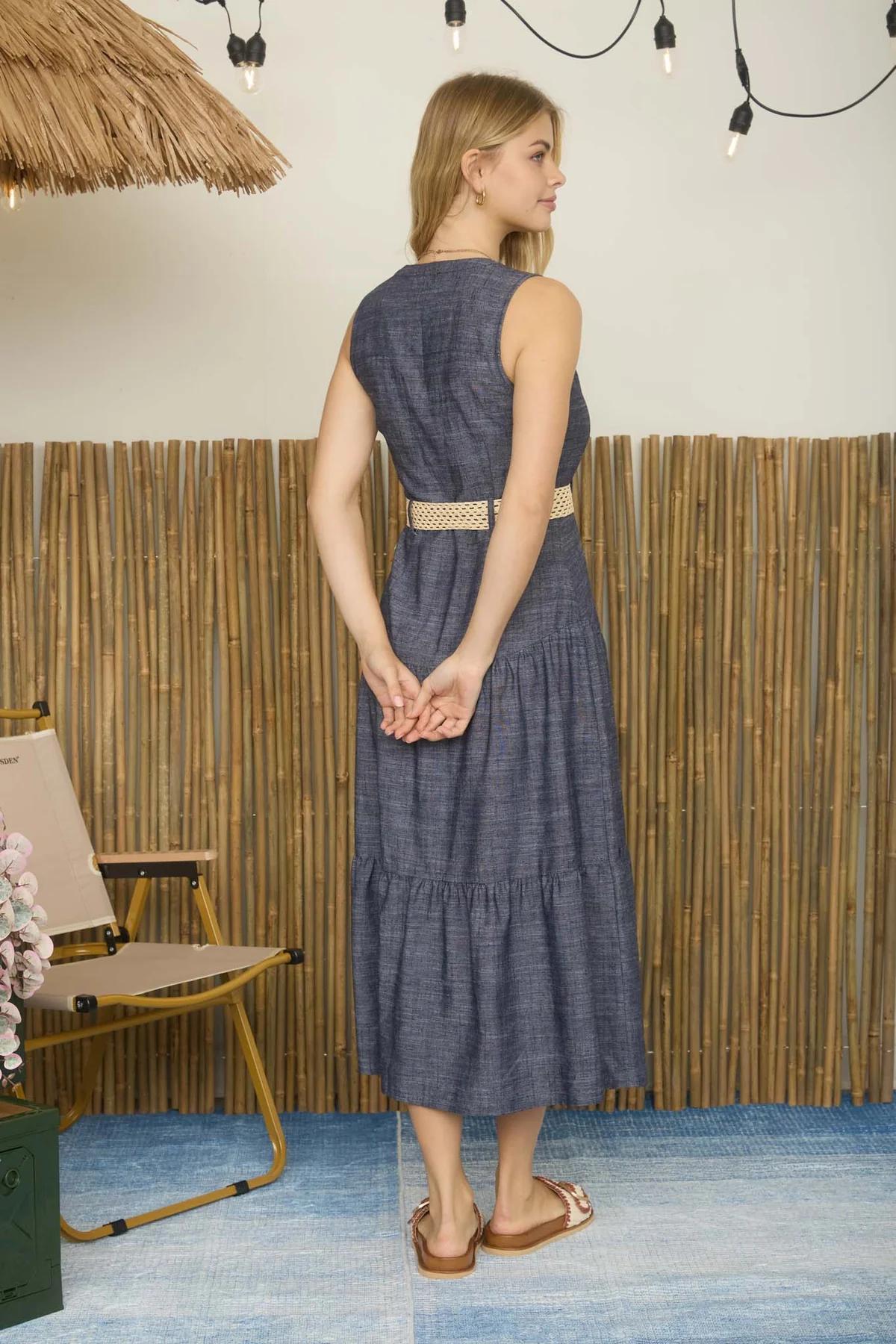 Woman in a blue dress standing in a room with a bamboo wall and straw ceiling.