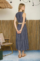 Woman in a blue dress standing in a room with a bamboo wall and straw ceiling.