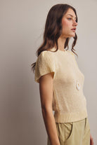 Woman wearing a light yellow knitted top against a plain background
