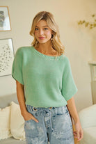 Woman wearing a green sweater and denim shorts in a living room setting