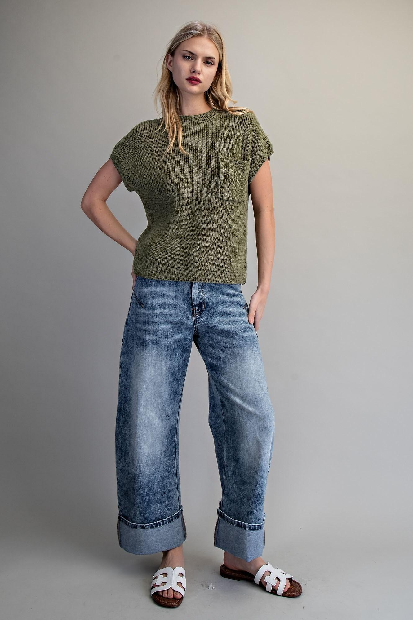 Woman wearing a green sweater and blue jeans against a gray background