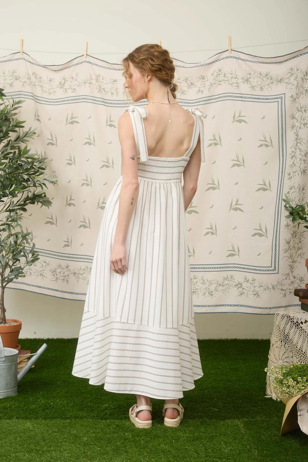 Woman in a white dress standing in front of a patterned wall.