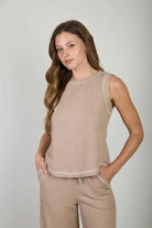 Woman wearing a beige sleeveless top and pants against a plain background