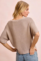 Woman wearing a beige knit sweater and blue jeans on a pink background