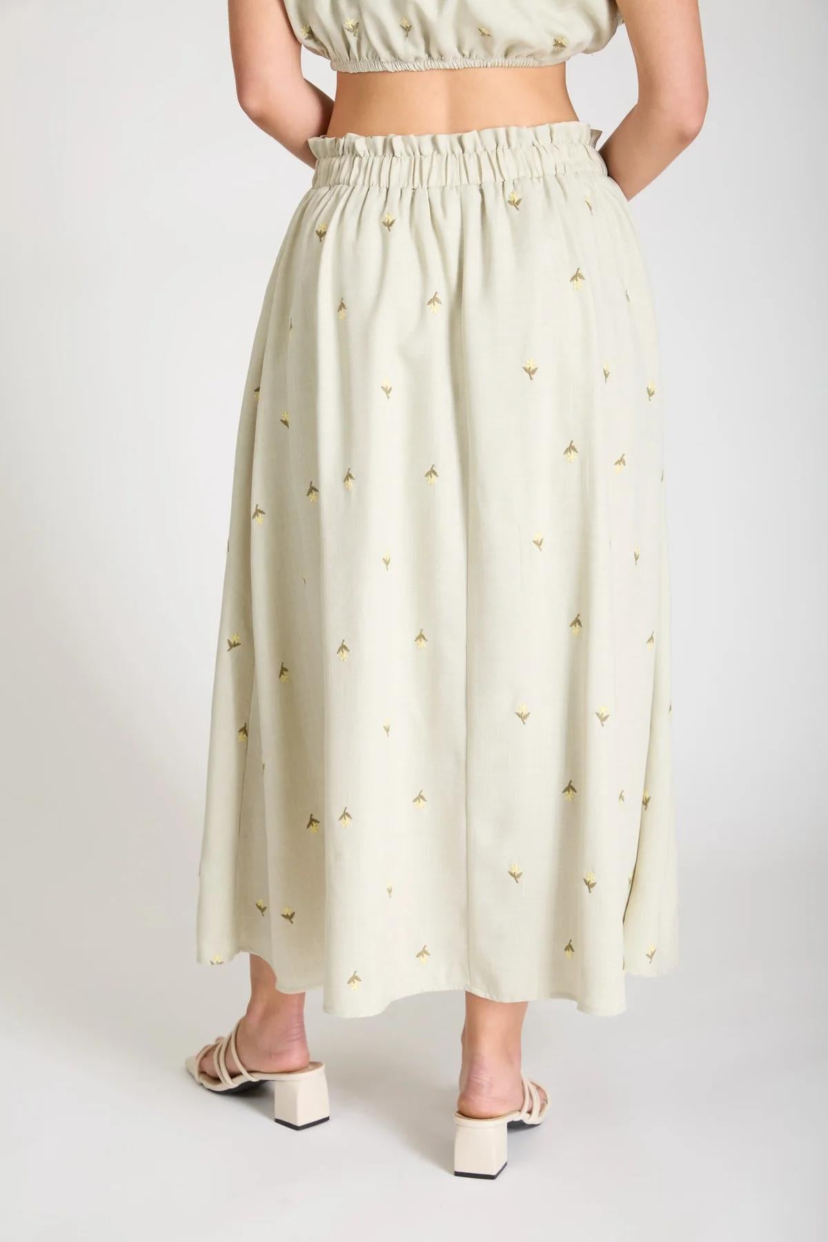 Person wearing a light-colored skirt with a subtle pattern on a plain background