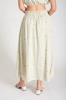 Person wearing a light-colored skirt with a subtle pattern on a plain background